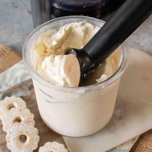 Pale vanilla ice cream being scooped from the Ninja pot in close up with small biscuits in the foreground