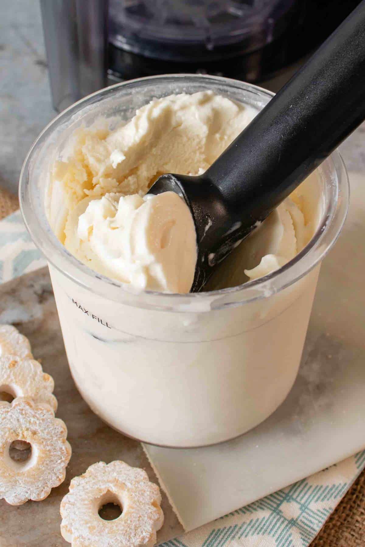 Ninja Creami vanilla ice cream being scooped from the pot. Small biscuits in the foreground.