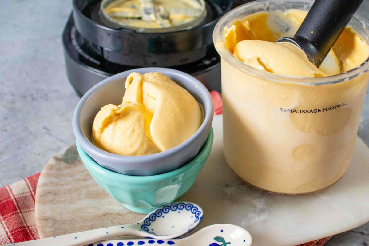 Passion fruit ice cream scoop in a small bowl and the Ninja Creami pot