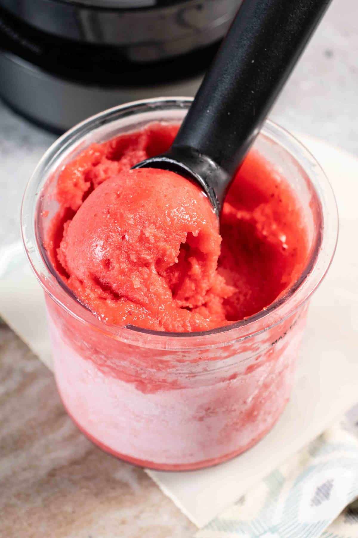 Scooping pale pink delicious strawberry sorbet from the Ninja Creami pot with a black ice cream scoop