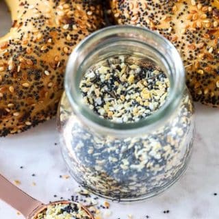 a jar of everything bagel seasoning with two freshly baked bagels