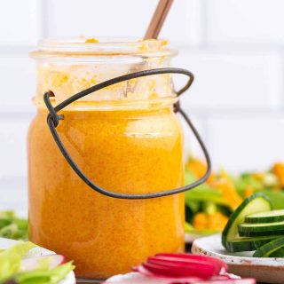 a glass jar of vibrant orange dressing surrounded by salad vegetables