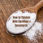 A top down view of a wooden spoon of white cornflour on a wood backdrop