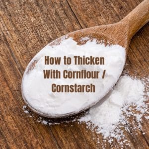 A top down view of a wooden spoon of white cornflour on a wood backdrop