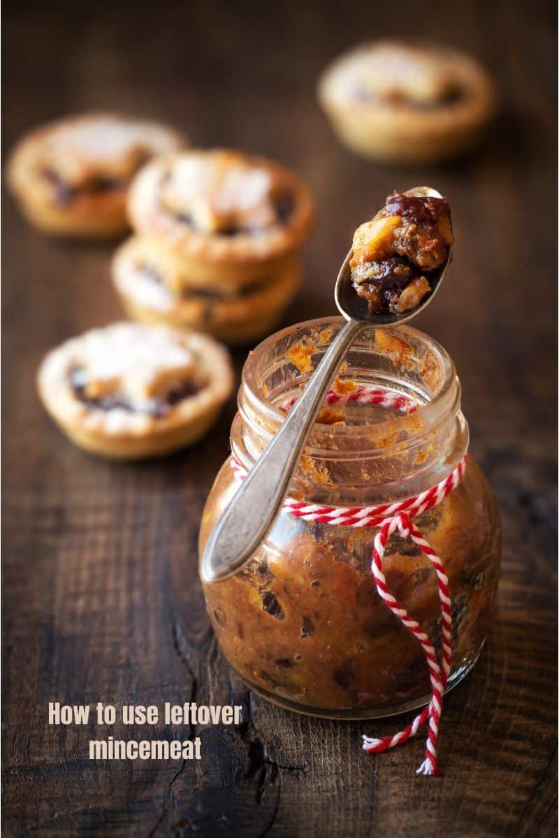 a spoon resting on a open jar of mincemeat with mincepies in the background