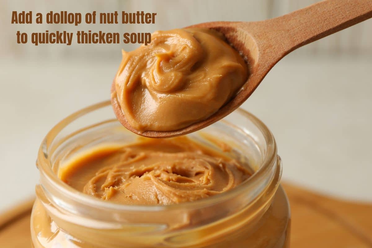 a close up of a wooden spoon scooping a dollop of peanut butter out of a jar