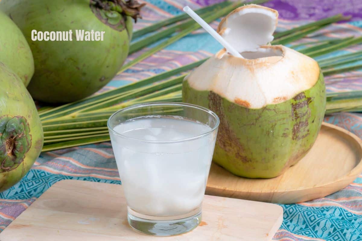 a glass of cloudy coconut water with an opened green coconut behind