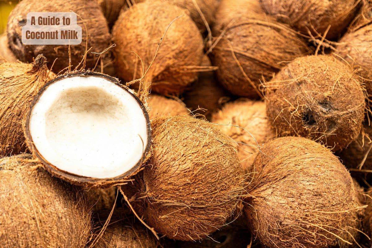 a pile of whole coconuts with one half one showing the white inside