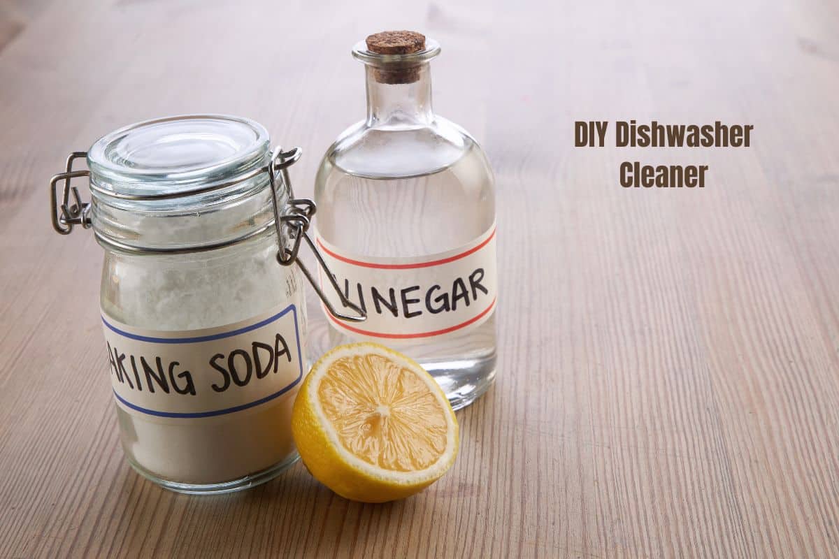 A bottle of vinegar, a clip top jar of baking soda and half a lemon, all on a wooden surface.