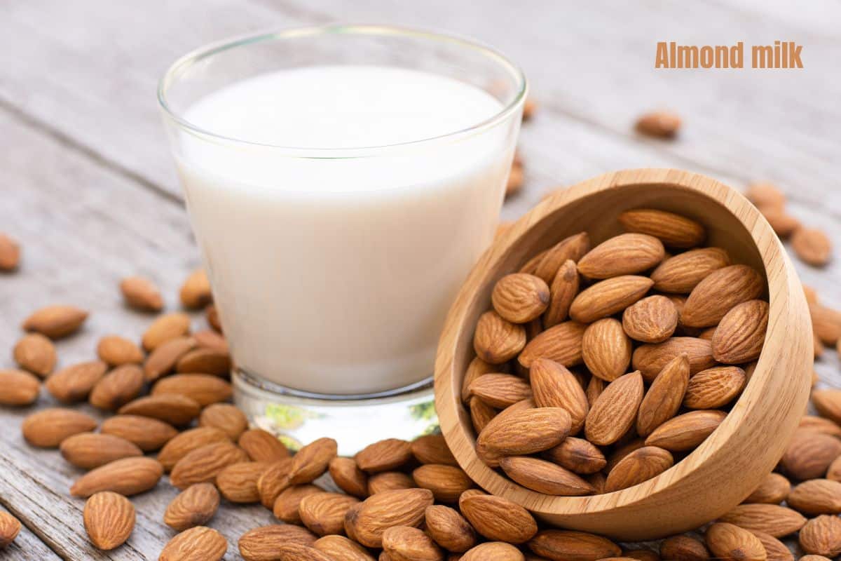 a glass of creamy white almond milk surrounded by whole almonds