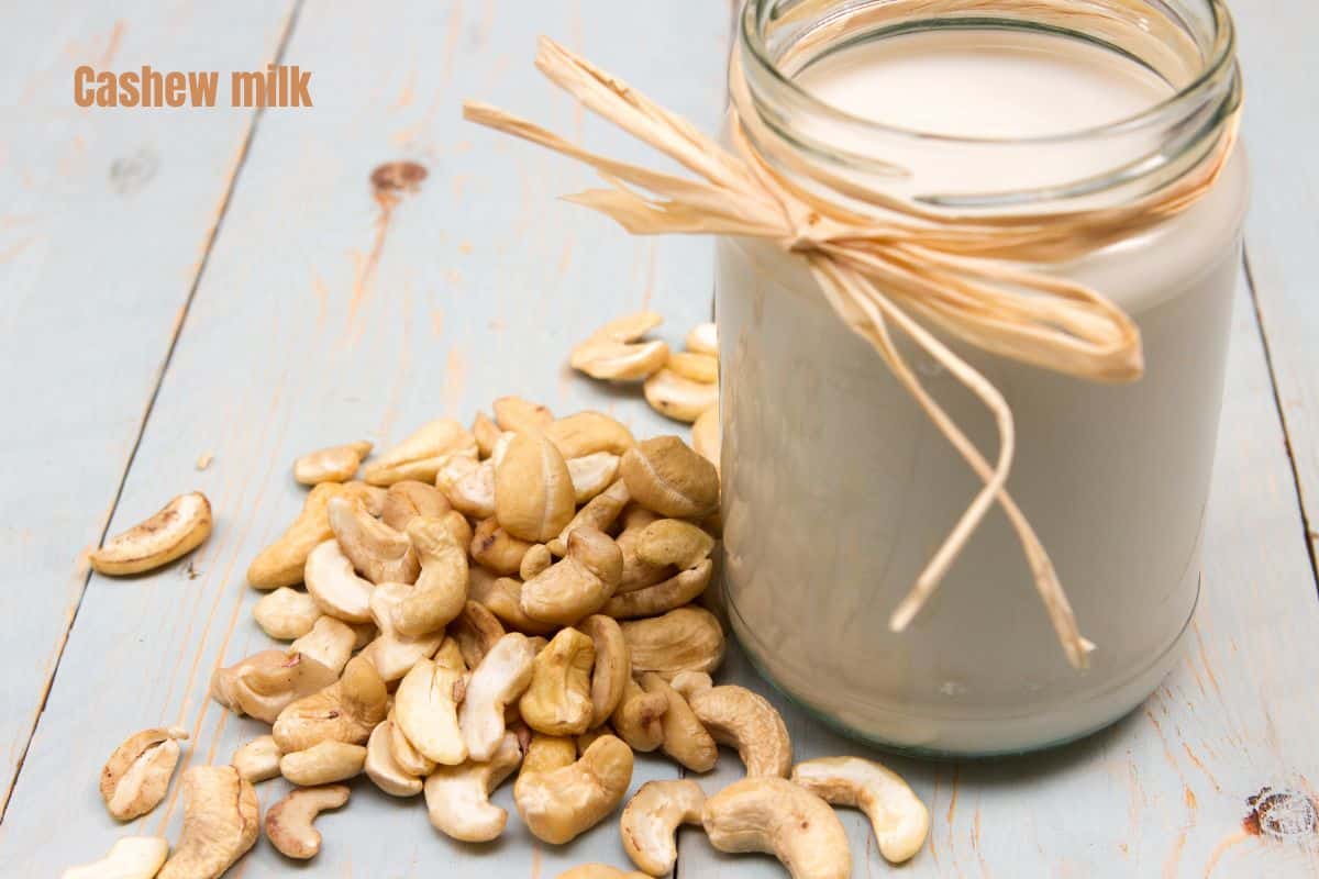a glass of creamy cashew milk surrounded by whole cashews