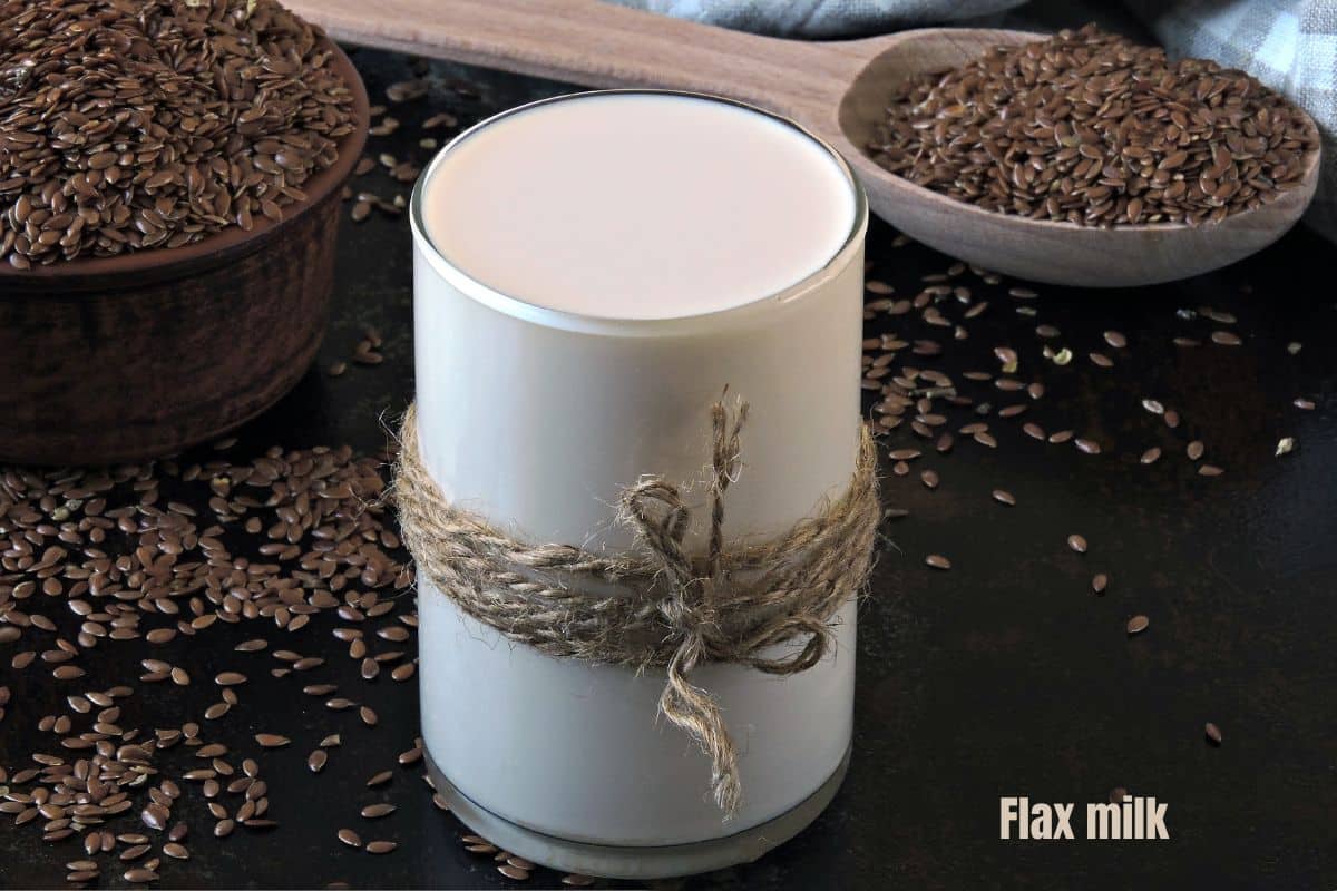 a glass of creamy white flax milk surrounded by whole flax seeds