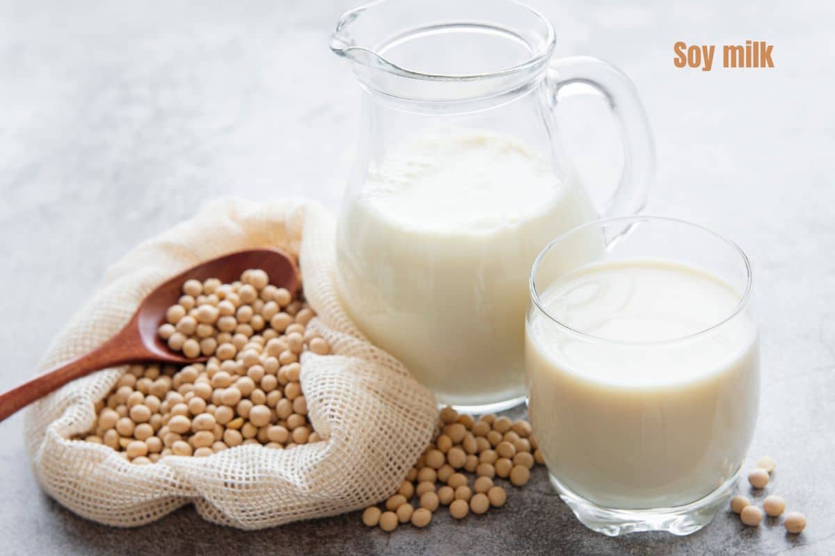 a jug and glass of soy milk next to a bag of taupe soy beans