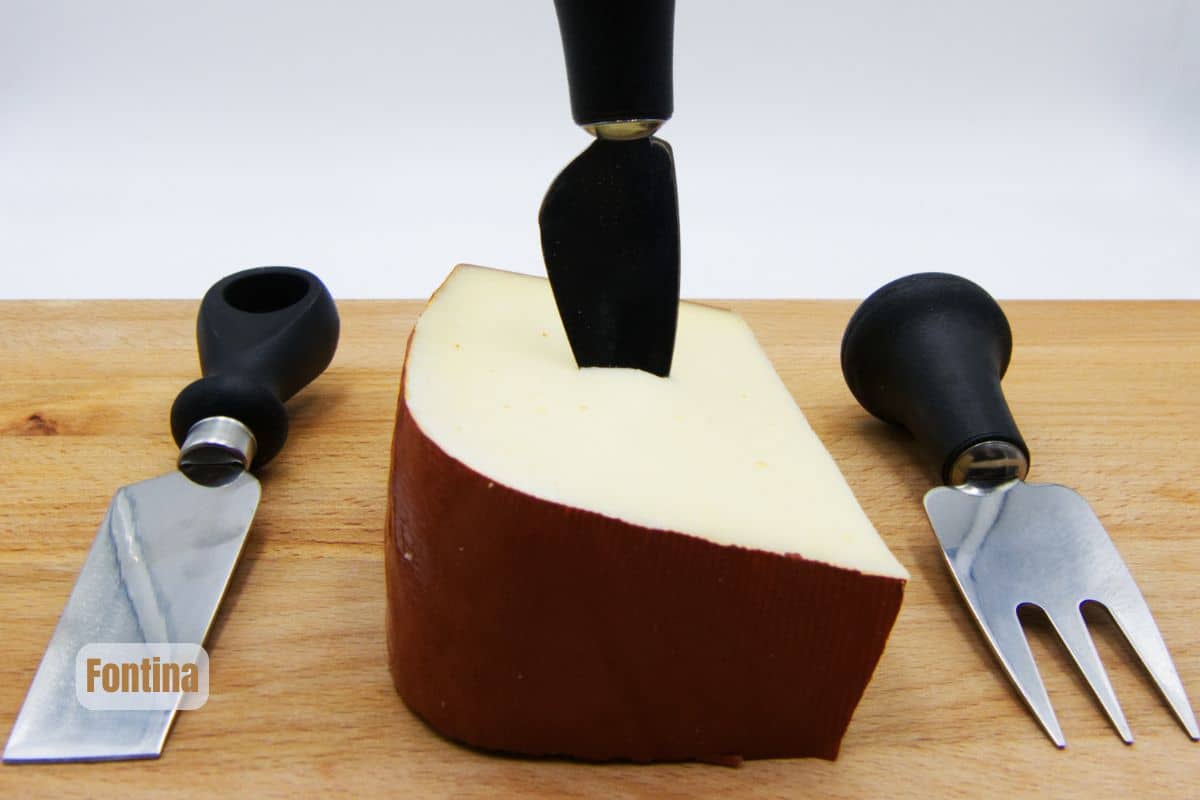 a piece of brown rinded fontina with cheese knives